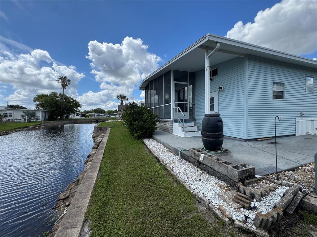 A light blue house with a screened porch sits beside a canal and concrete patio — 35151 DANNY DRIVE Lot 114, ZEPHYRHILLS, FL