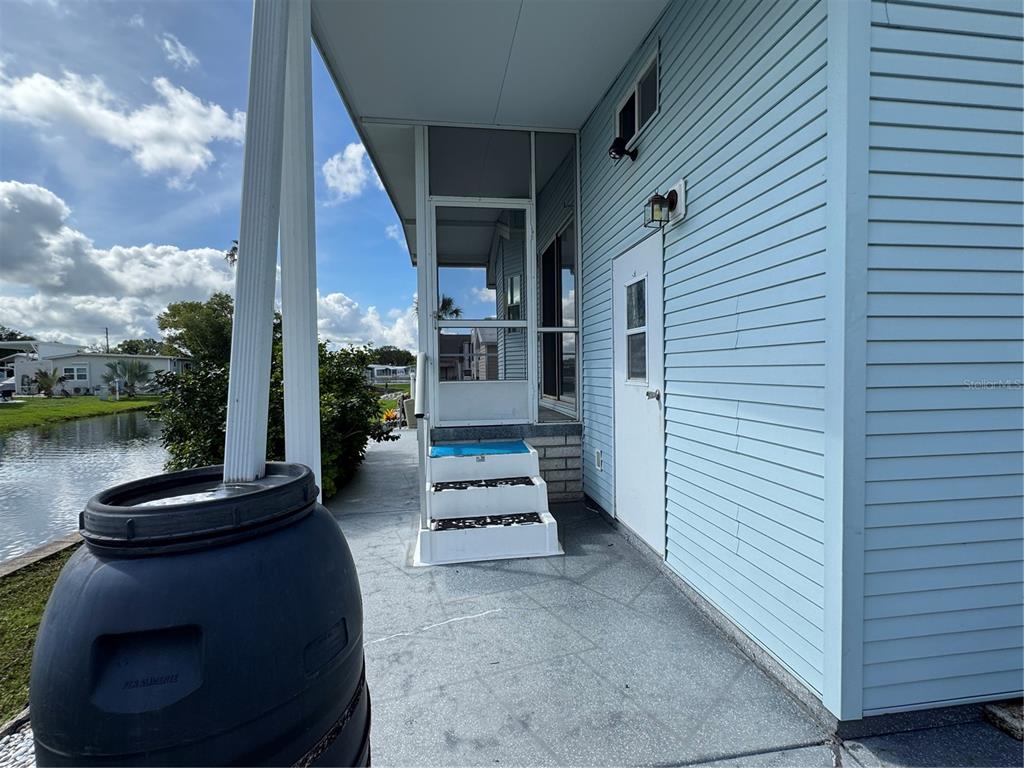 A view of a light blue mobile home exterior with a screened porch and rain barrel — 35151 DANNY DRIVE Lot 114, ZEPHYRHILLS, FL