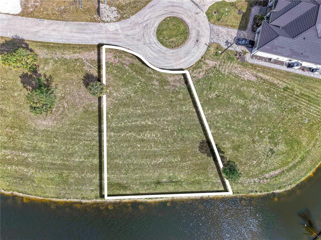 An aerial view shows a vacant, trapezoidal residential lot bordering a curved road and water — 16299 CAYMAN LANE, PUNTA GORDA, FL