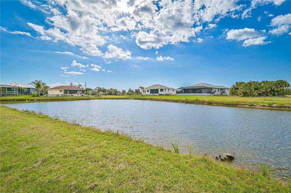 A grassy lawn slopes down to a pond with several houses in the background — 16299 CAYMAN LANE, PUNTA GORDA, FL
