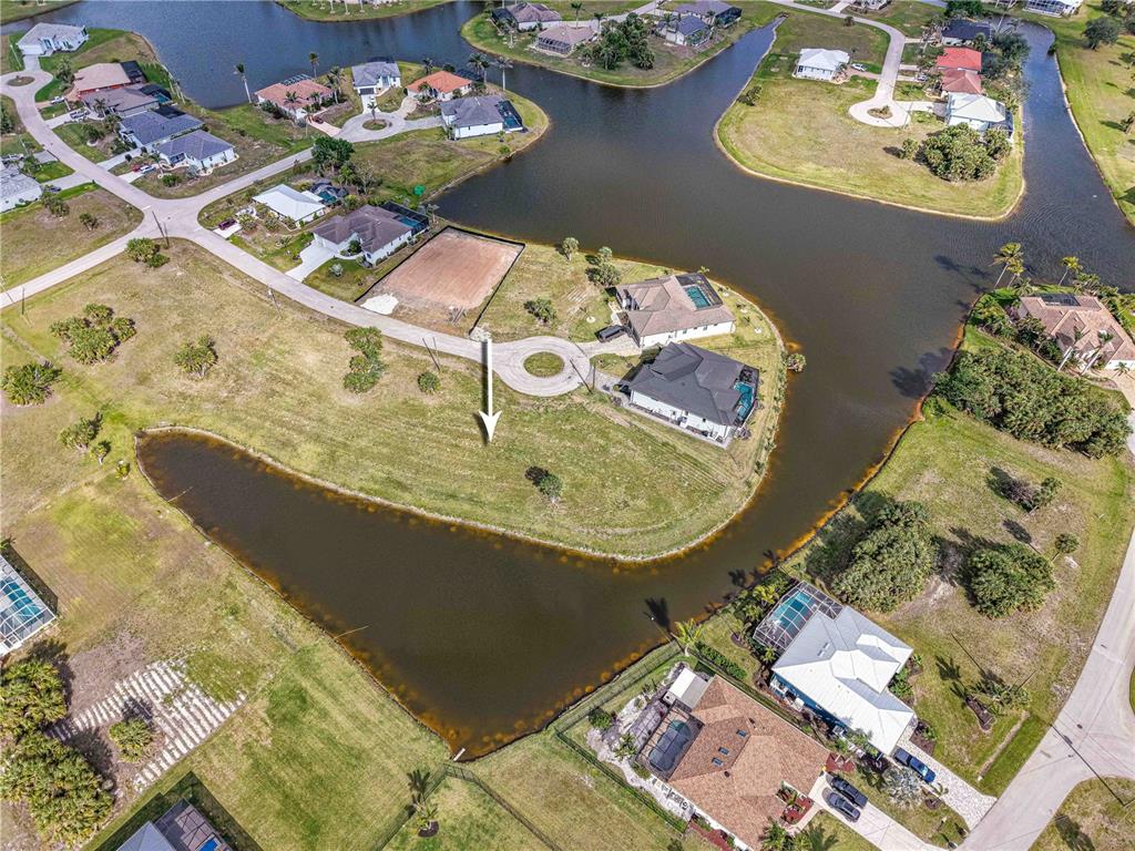 An aerial view shows a vacant, grassy residential lot situated on a curved waterfront — 16299 CAYMAN LANE, PUNTA GORDA, FL
