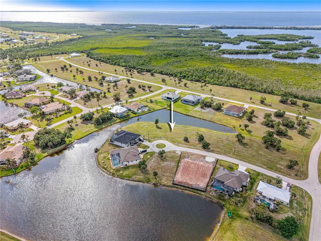 An aerial view shows a vacant residential lot situated next to a pond and houses — 16299 CAYMAN LANE, PUNTA GORDA, FL