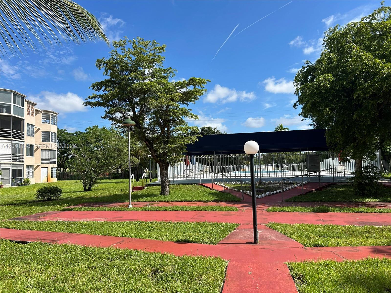 A red walkway leads toward a fenced swimming pool area next to a residential building — 1501 NE 191st St # C401, Miami FL 33179, MIAMI, FL