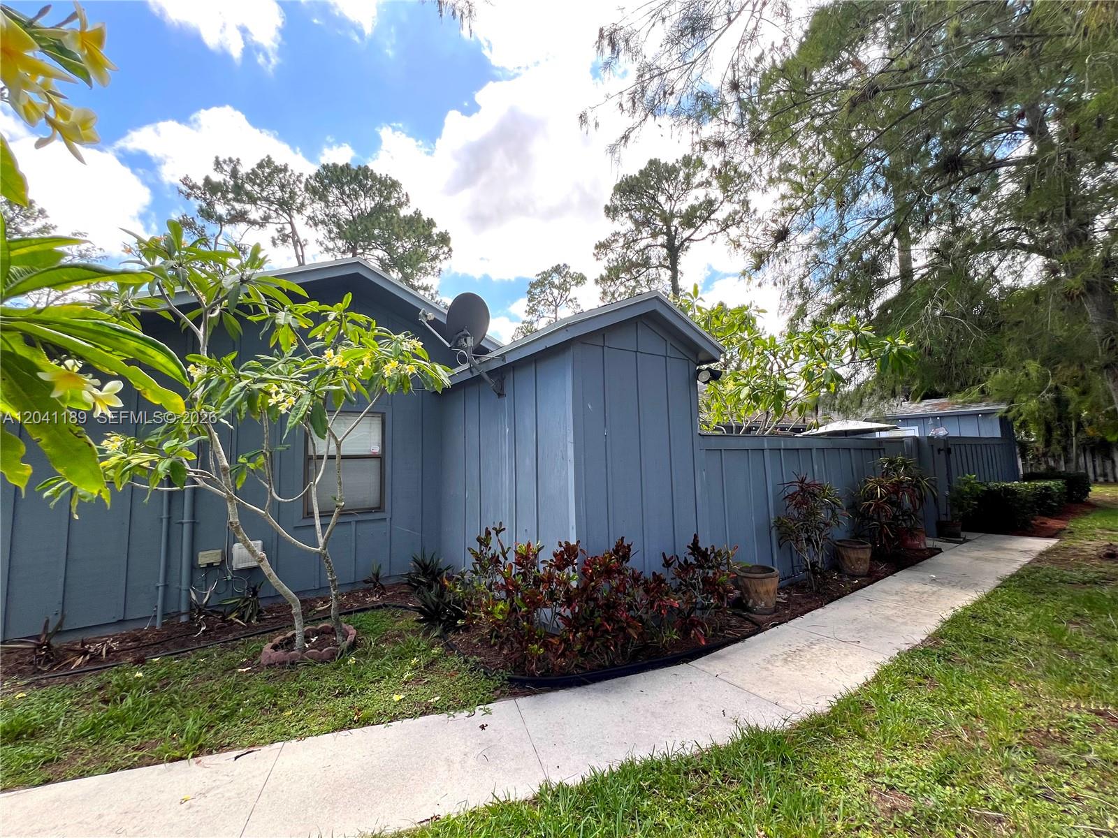 A blue house exterior features a concrete walkway, landscaping, and a satellite dish — 1077 Goldenrod Rd # 1077, Wellington FL 33414, WELLINGTON, FL