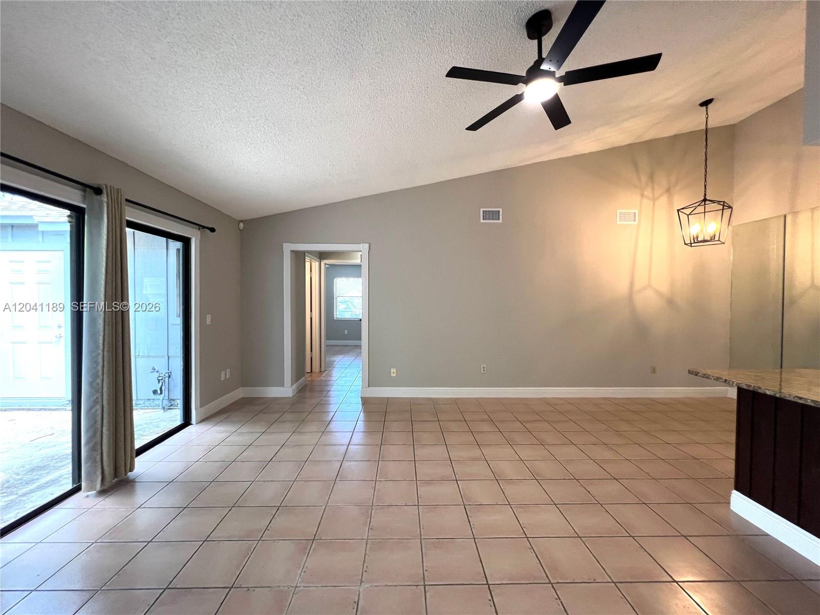 An open-concept living area features vaulted ceilings, tile flooring, a ceiling fan, and sliding doors — 1077 Goldenrod Rd # 1077, Wellington FL 33414, WELLINGTON, FL
