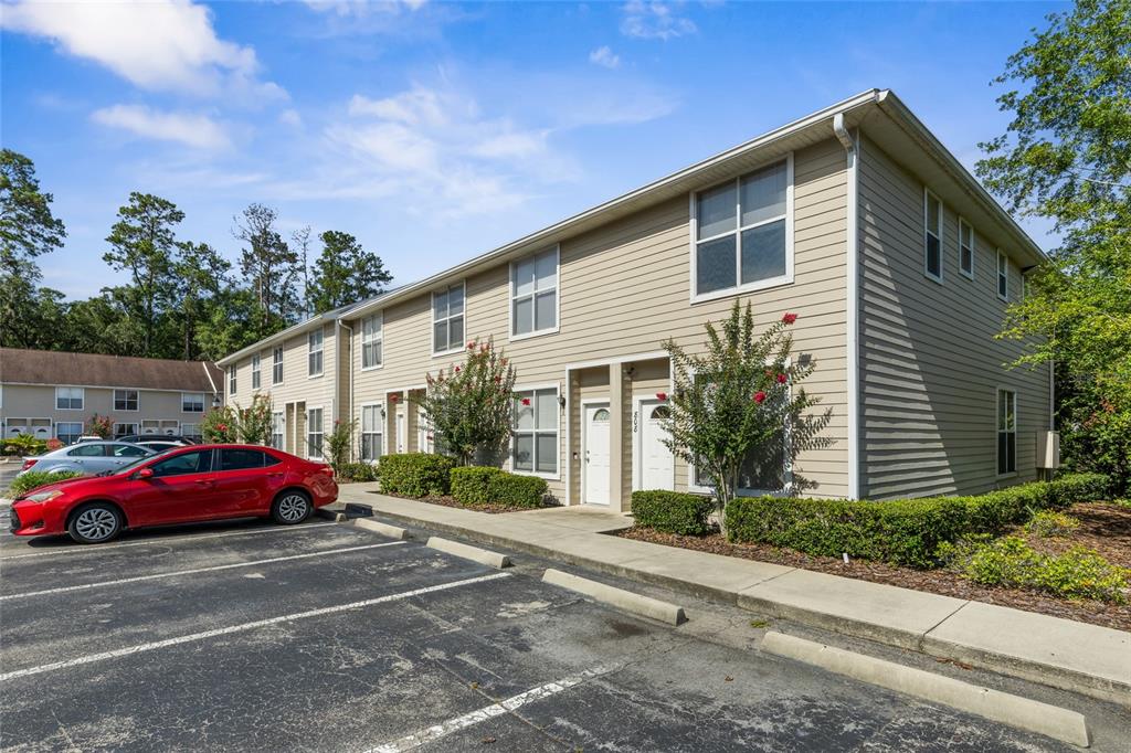 A two-story apartment building with tan siding and a parking lot in the foreground — 3901 SW 20TH AVENUE UNIT 806, GAINESVILLE, FL