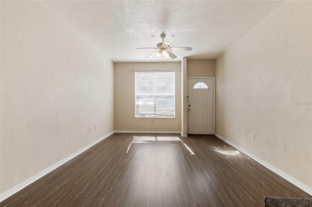 An empty living room with wood-look flooring, a ceiling fan, a window, and a door — 3901 SW 20TH AVENUE UNIT 806, GAINESVILLE, FL