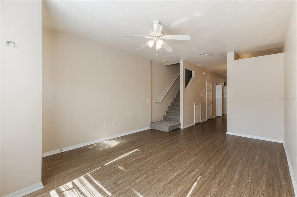 An empty living room features wood-look flooring, a ceiling fan, and stairs leading upward — 3901 SW 20TH AVENUE UNIT 806, GAINESVILLE, FL