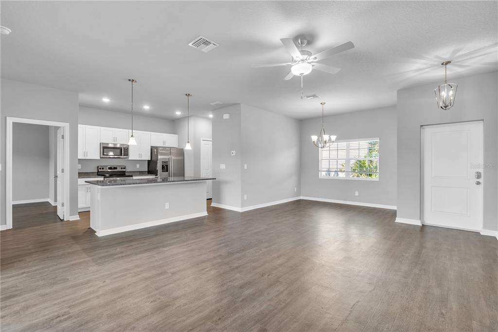 An open-concept kitchen and dining area with white cabinets, stainless appliances, and wood-look flooring — 5289 GILLOT BOULEVARD, PORT CHARLOTTE, FL