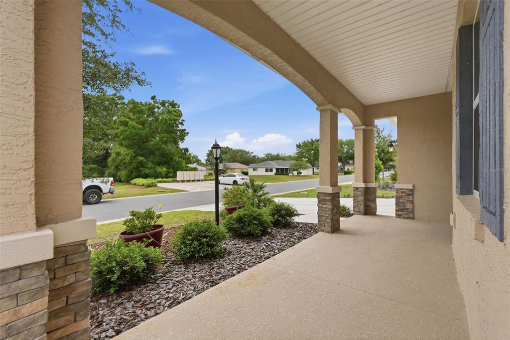 A covered front porch features stone-based columns, a concrete floor, and a view of landscaping — 9958 SW 97TH LANE, OCALA, FL
