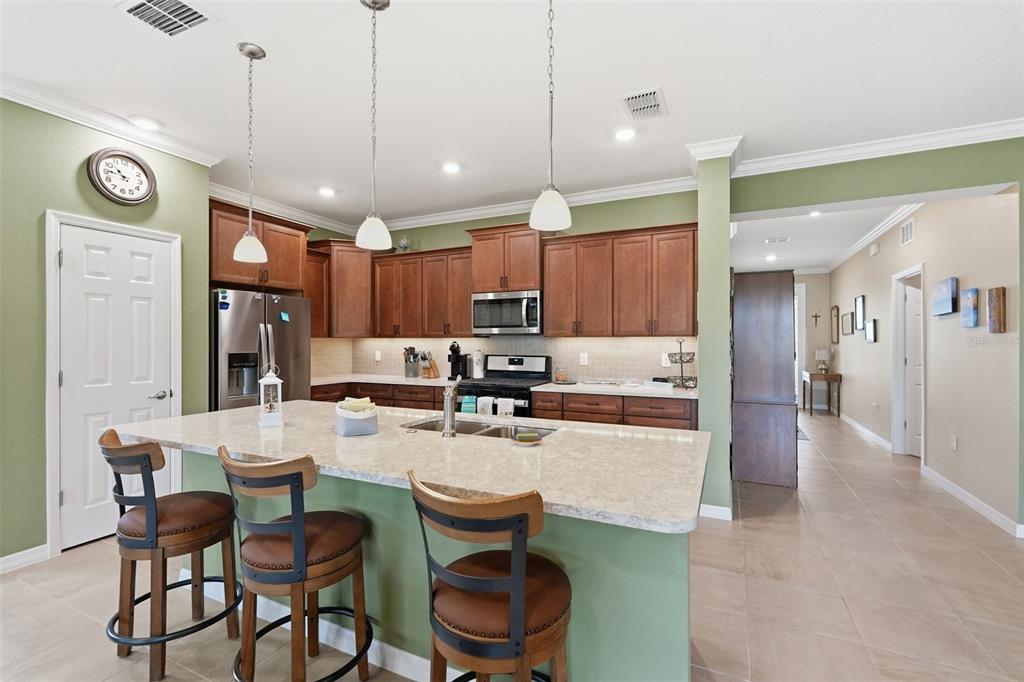 A kitchen features a large island with bar stools, wooden cabinets, and light-colored countertops — 9958 SW 97TH LANE, OCALA, FL
