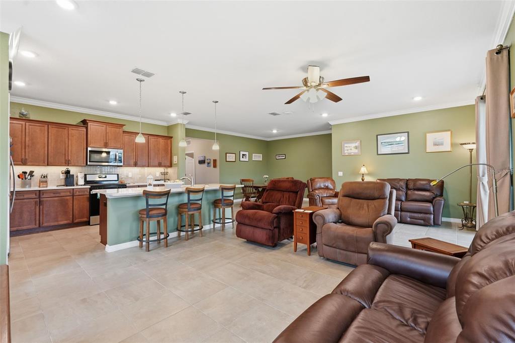 An open-concept kitchen and living area with brown cabinetry, tile floors, and leather furniture — 9958 SW 97TH LANE, OCALA, FL
