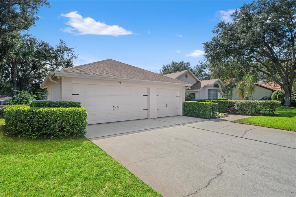 A beige house with a two-car garage and a concrete driveway sits behind manicured hedges — 15923 ELLSWORTH DRIVE, TAMPA, FL