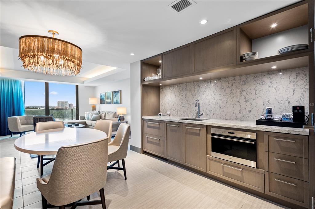 A modern kitchenette with wood cabinetry and marble countertops sits beside a dining area — 691 S GULFVIEW BOULEVARD UNIT 1211, CLEARWATER BEACH, FL