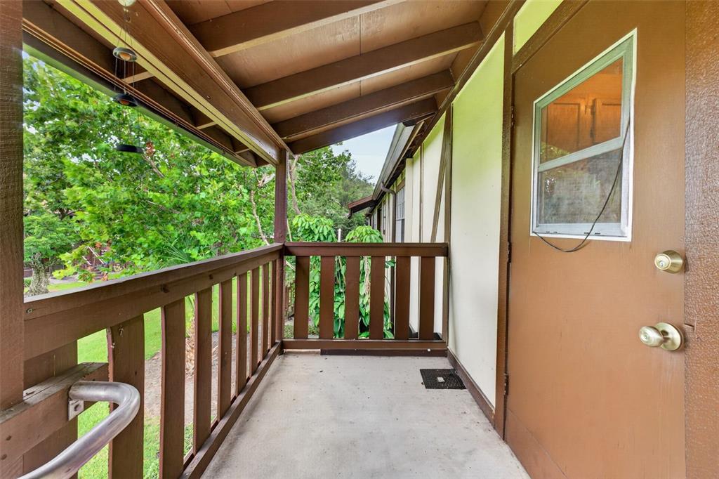A covered outdoor balcony features a brown wooden railing, concrete flooring, and a brown door — 5301 HANSEL AVENUE UNIT A-18, EDGEWOOD, FL