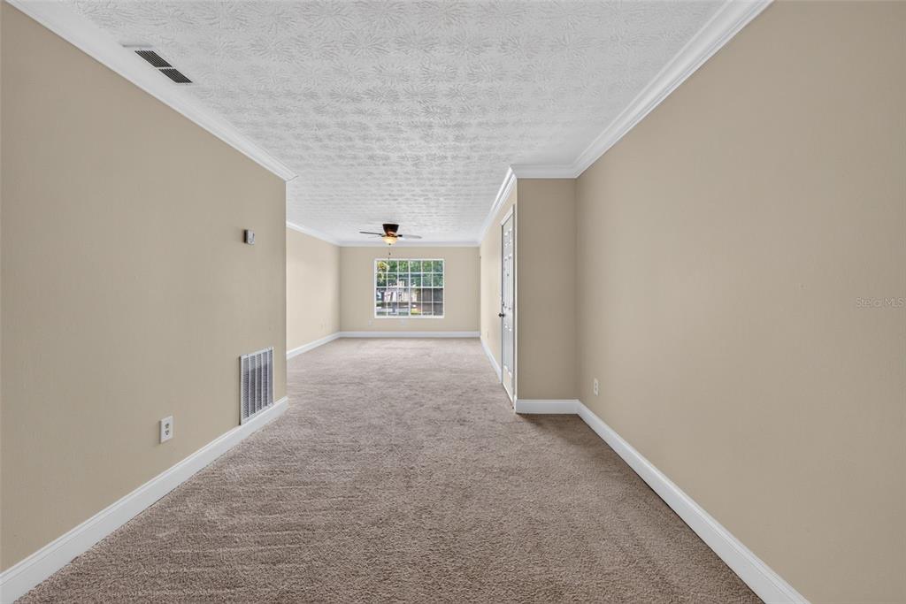 A long, carpeted room with beige walls, a textured ceiling, and a single window — 5301 HANSEL AVENUE UNIT A-18, EDGEWOOD, FL