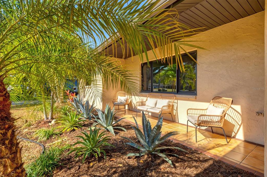 A covered patio features tiled flooring, wicker furniture, and desert landscaping in front of a house — 2641 HYDE PARK STREET, SARASOTA, FL
