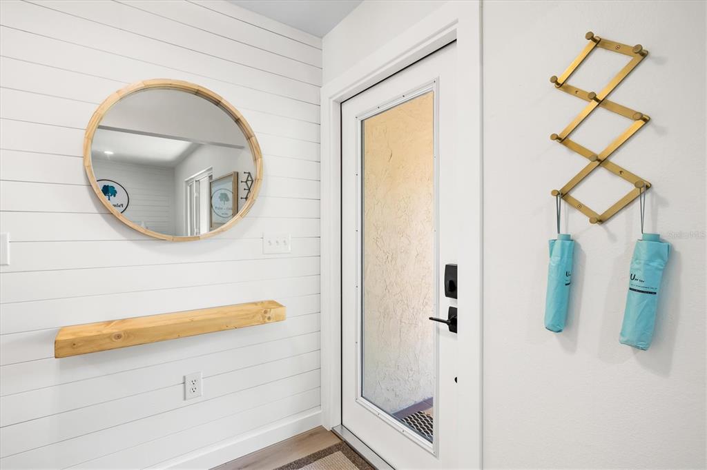 An entryway features white shiplap walls, a round mirror, a wooden shelf, and a wall-mounted rack — 2641 HYDE PARK STREET, SARASOTA, FL