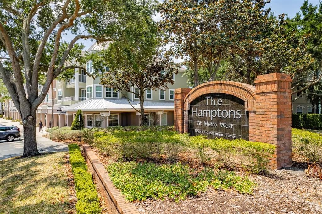A brick sign for The Hamptons at Metro West stands before a multi-story apartment building — 6648 TIME SQUARE AVENUE UNIT 105, ORLANDO, FL