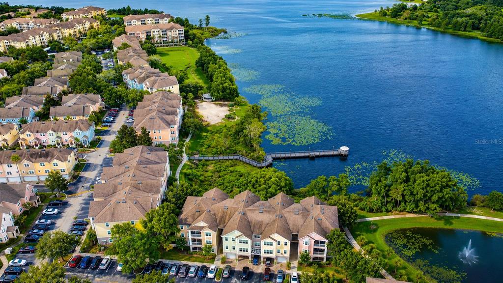 An aerial view shows multi-story residential townhomes situated along a lake with a wooden pier — 6648 TIME SQUARE AVENUE UNIT 105, ORLANDO, FL