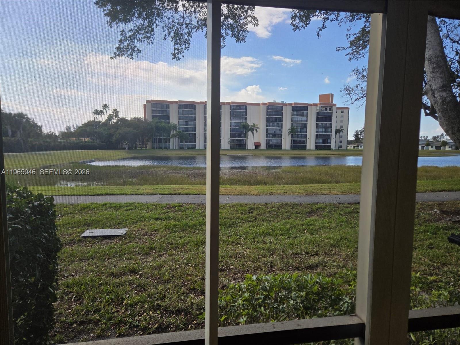 A view of a pond and a multi-story apartment building seen through a screened enclosure — 6675 S Oriole Blvd # 1040, Delray Beach FL 33446, DELRAY BEACH, FL