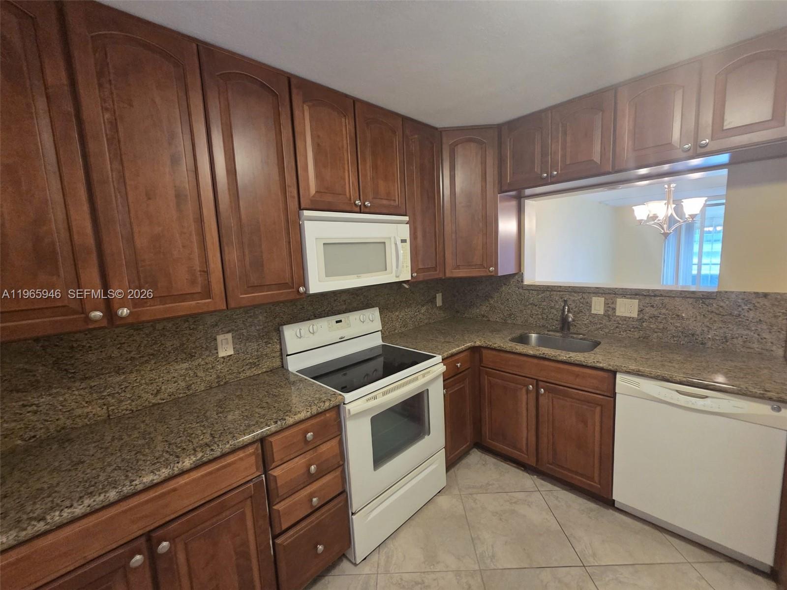 A kitchen features wood cabinets, granite countertops, white appliances, and tile flooring — 6675 S Oriole Blvd # 1040, Delray Beach FL 33446, DELRAY BEACH, FL