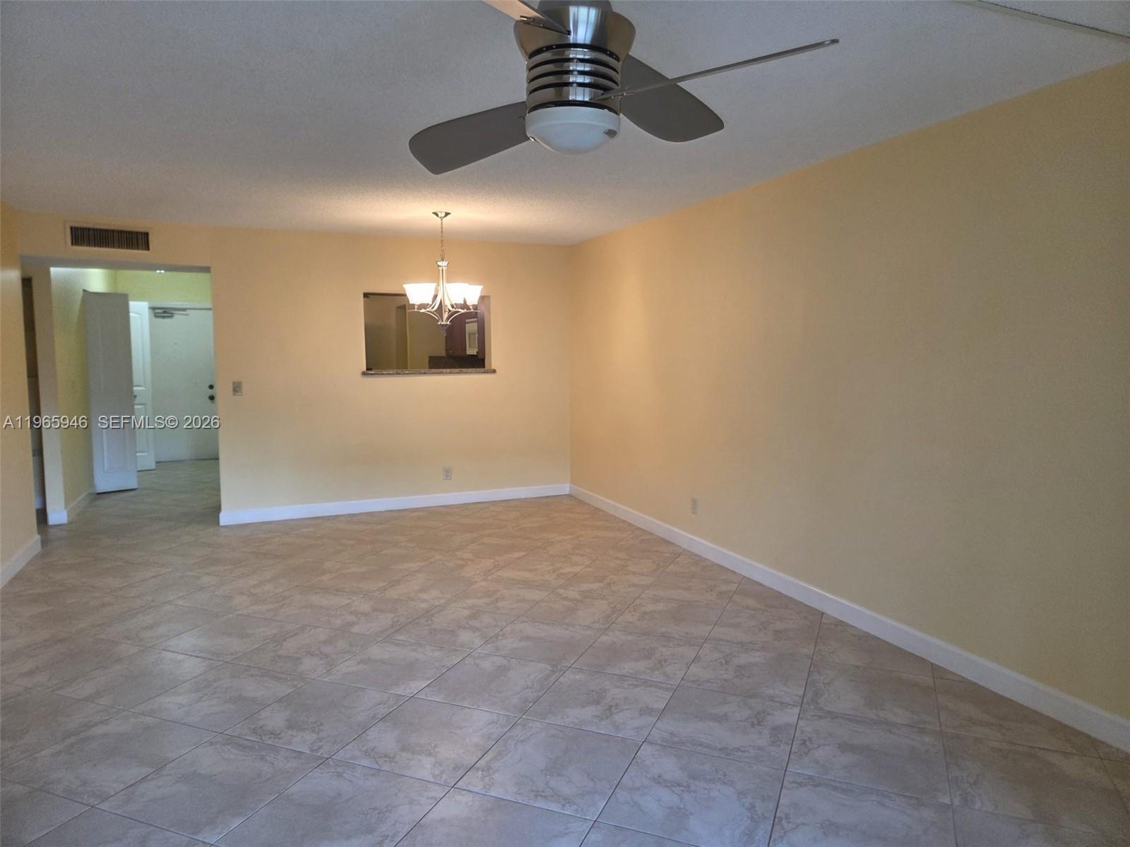 An empty living room features light yellow walls, tile flooring, a ceiling fan, and a chandelier — 6675 S Oriole Blvd # 1040, Delray Beach FL 33446, DELRAY BEACH, FL