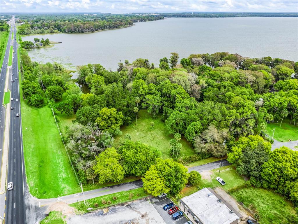 An aerial view shows a wooded lot situated between a highway and a large lake — S US HWY 27 & HOWARD RD, LEESBURG, FL