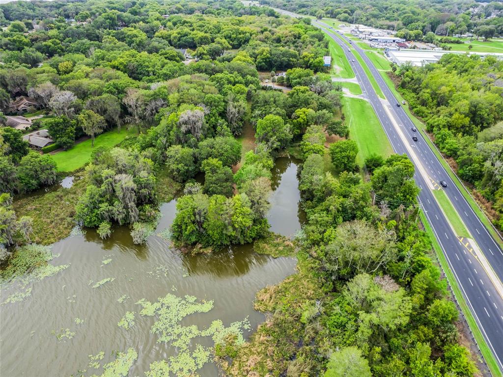 An aerial view shows a wooded lot with a pond adjacent to a multi-lane highway — S US HWY 27 & HOWARD RD, LEESBURG, FL