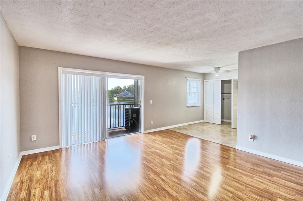 A living room with wood-look flooring, a sliding glass door to a balcony, and a closet — 13760 ORANGE SUNSET DRIVE UNIT 201, TAMPA, FL