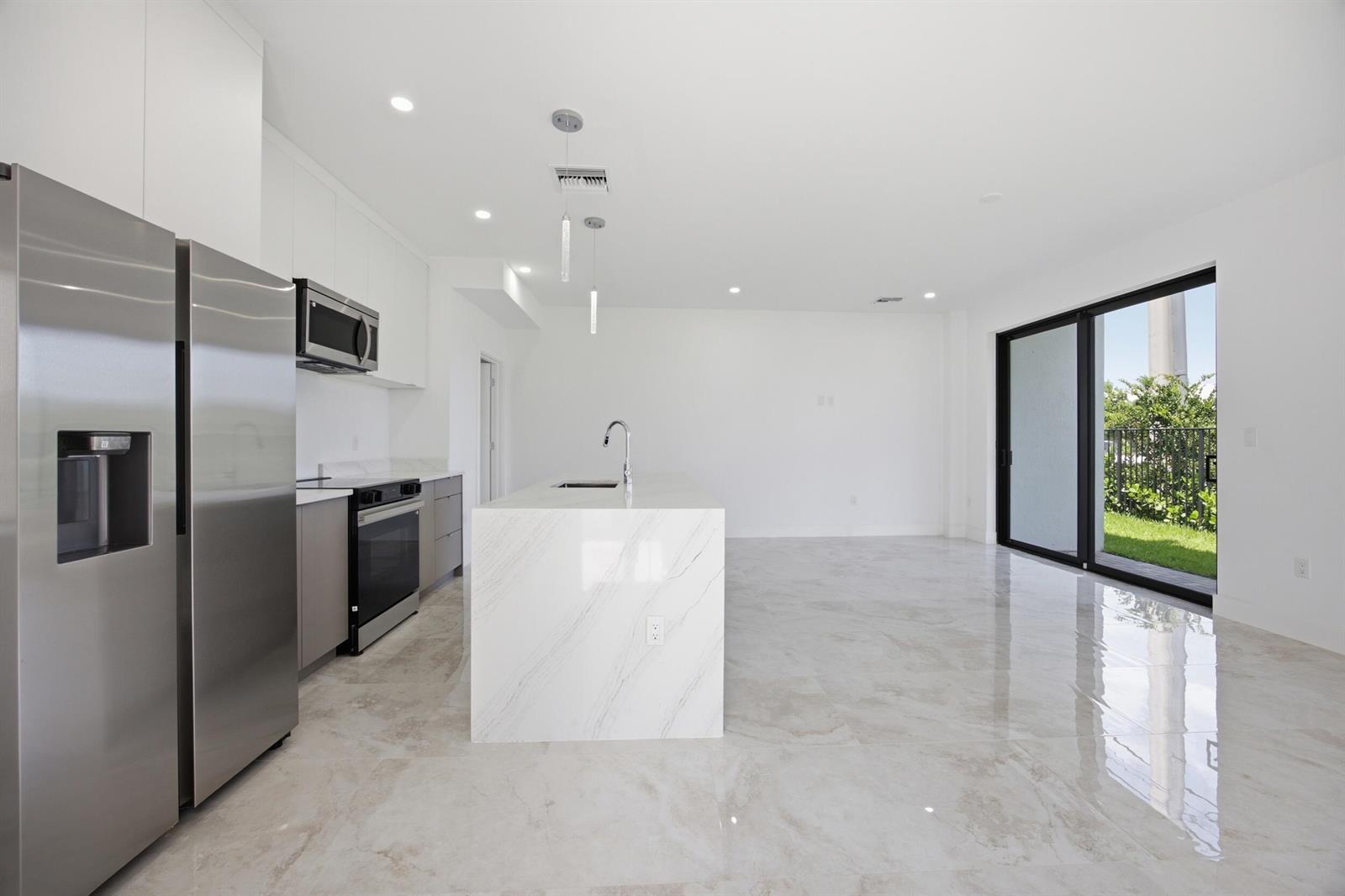 A modern kitchen features a marble island, stainless steel appliances, and large sliding glass doors — 1542 NW 1st Avenue, Pompano Beach FL 33060, POMPANO BEACH, FL
