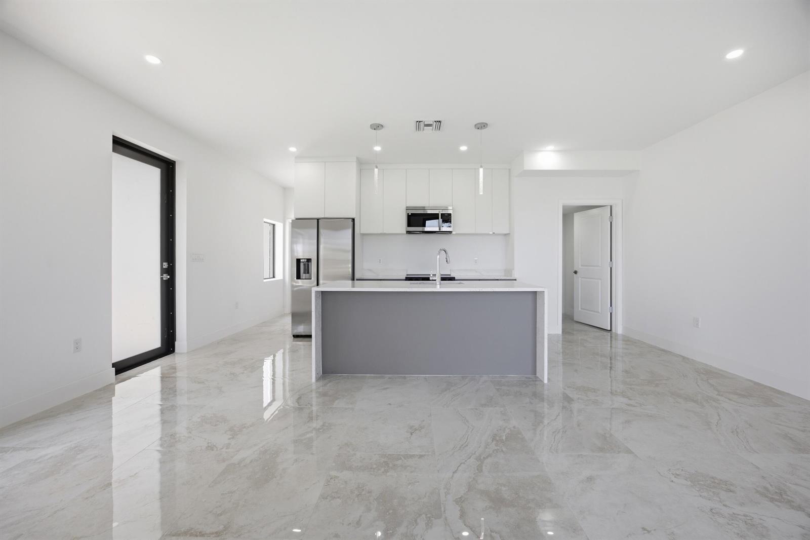 A modern kitchen features white cabinetry, a gray island, and polished marble-style tile flooring — 1542 NW 1st Avenue, Pompano Beach FL 33060, POMPANO BEACH, FL