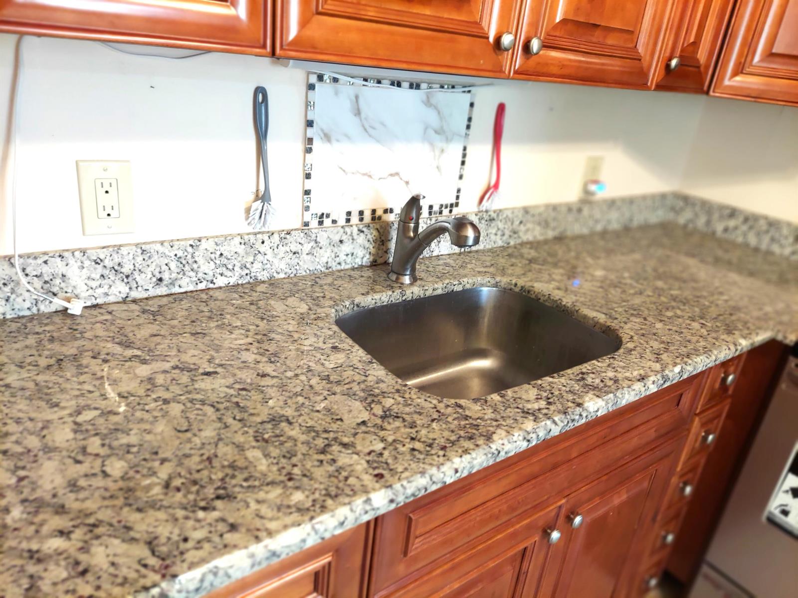 A kitchen sink with a stainless steel faucet set in granite countertops and wood cabinets — 3020 Ashby D, Deerfield Beach FL 33442, DEERFIELD BEACH, FL