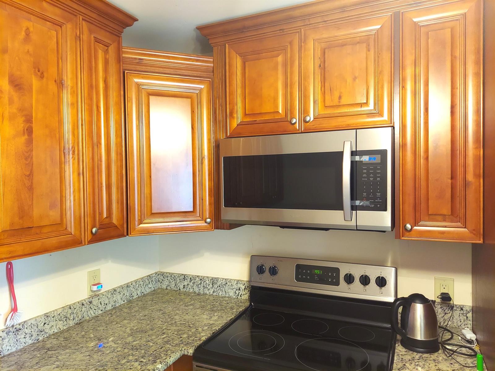 A kitchen corner features wood cabinets, a stainless steel microwave, and a black electric stove — 3020 Ashby D, Deerfield Beach FL 33442, DEERFIELD BEACH, FL