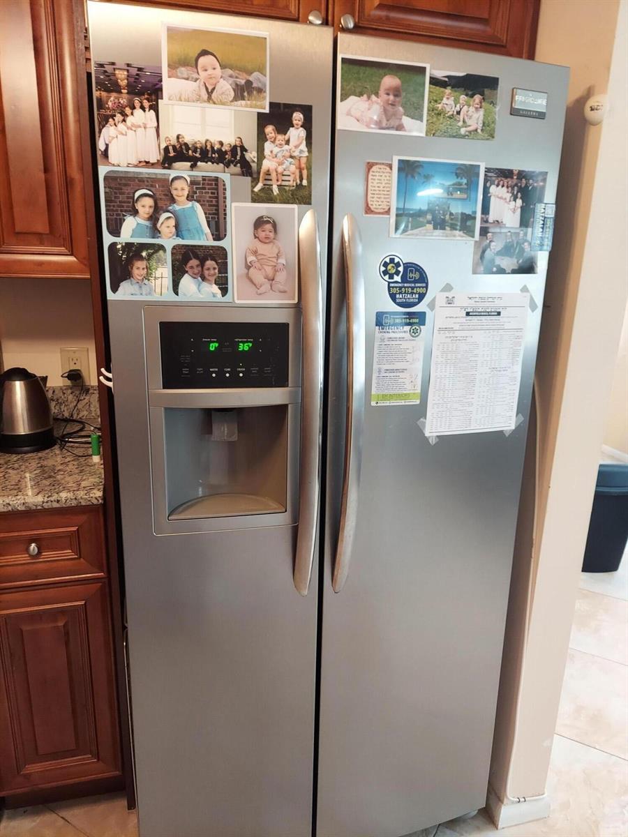 A stainless steel side-by-side refrigerator covered in photos stands in a kitchen with wood cabinets — 3020 Ashby D, Deerfield Beach FL 33442, DEERFIELD BEACH, FL