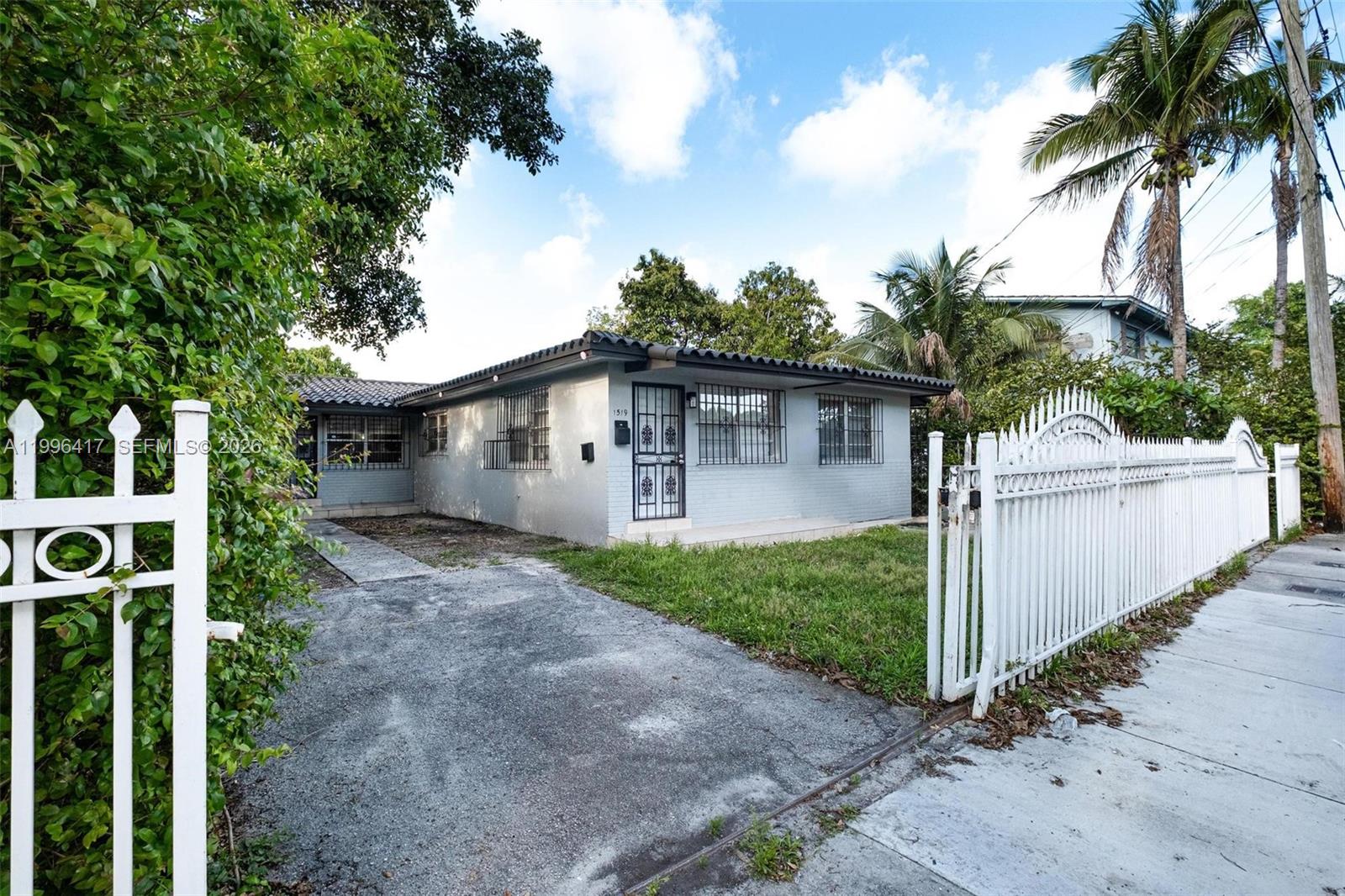 A single-story gray house with a tiled roof sits behind a white metal fence — 1519 NW 40th St, Miami FL 33142, MIAMI, FL