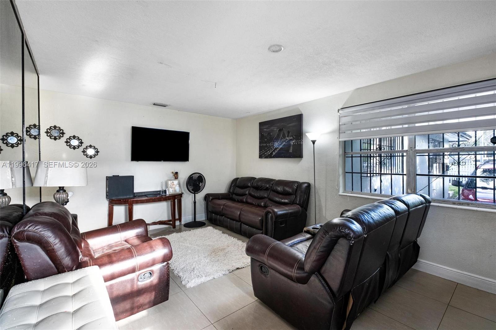 A living room features brown leather furniture, a wall-mounted television, and tile flooring — 1519 NW 40th St, Miami FL 33142, MIAMI, FL
