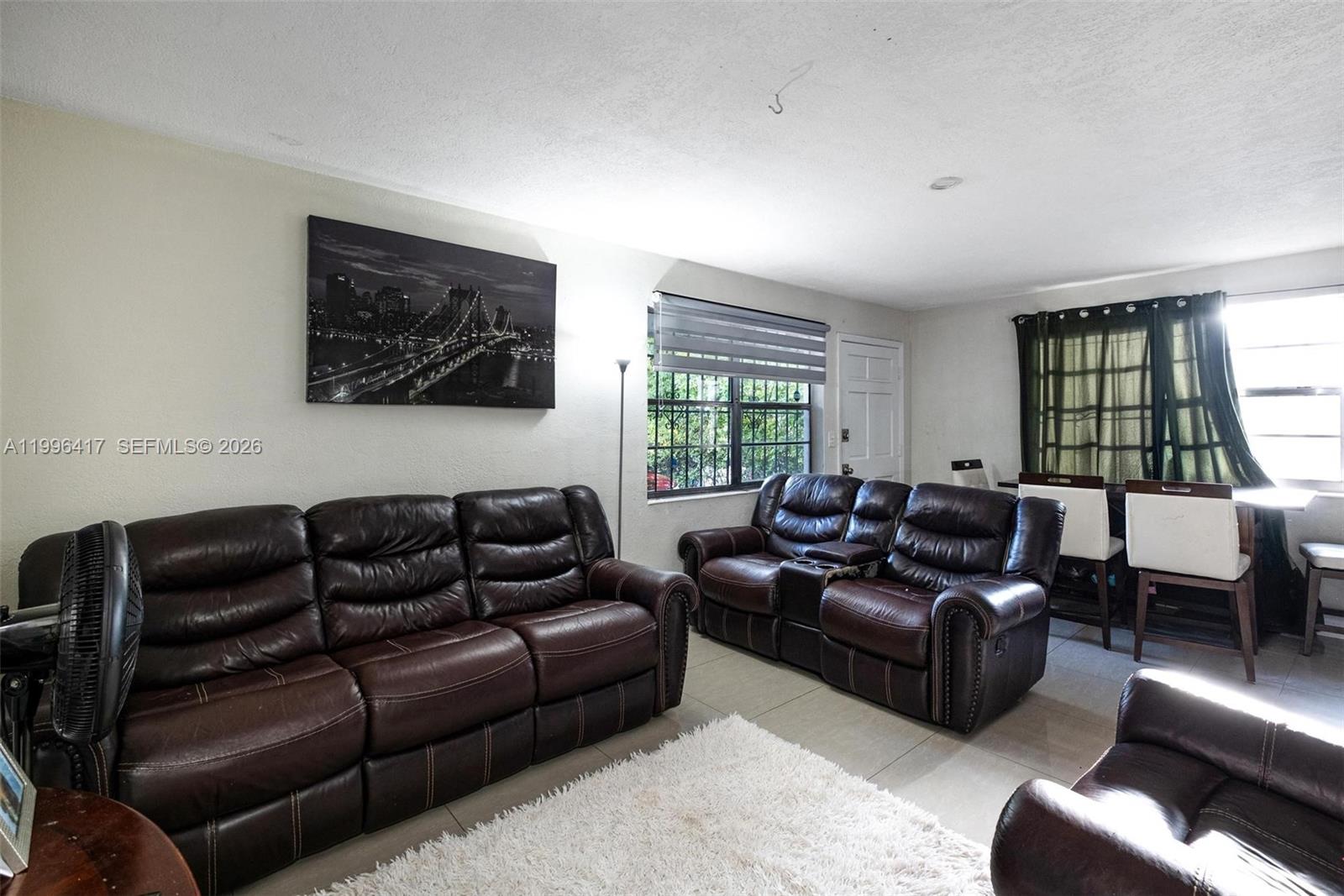 A living room features brown leather sofas, a white rug, and a wall-mounted bridge print — 1519 NW 40th St, Miami FL 33142, MIAMI, FL