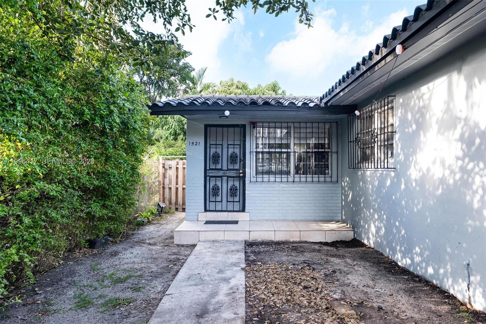 The exterior of a light blue brick house features a tiled porch and security bars — 1519 NW 40th St, Miami FL 33142, MIAMI, FL