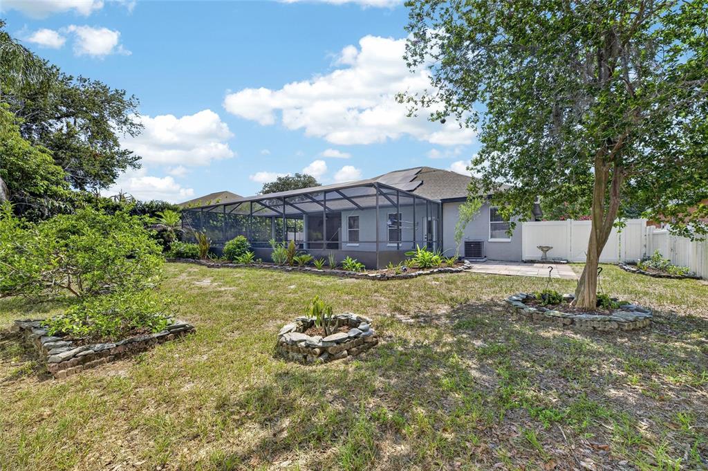 A backyard view of a house with a screened-in pool enclosure and stone-bordered garden beds — 10409 HARVESTIME PLACE, RIVERVIEW, FL