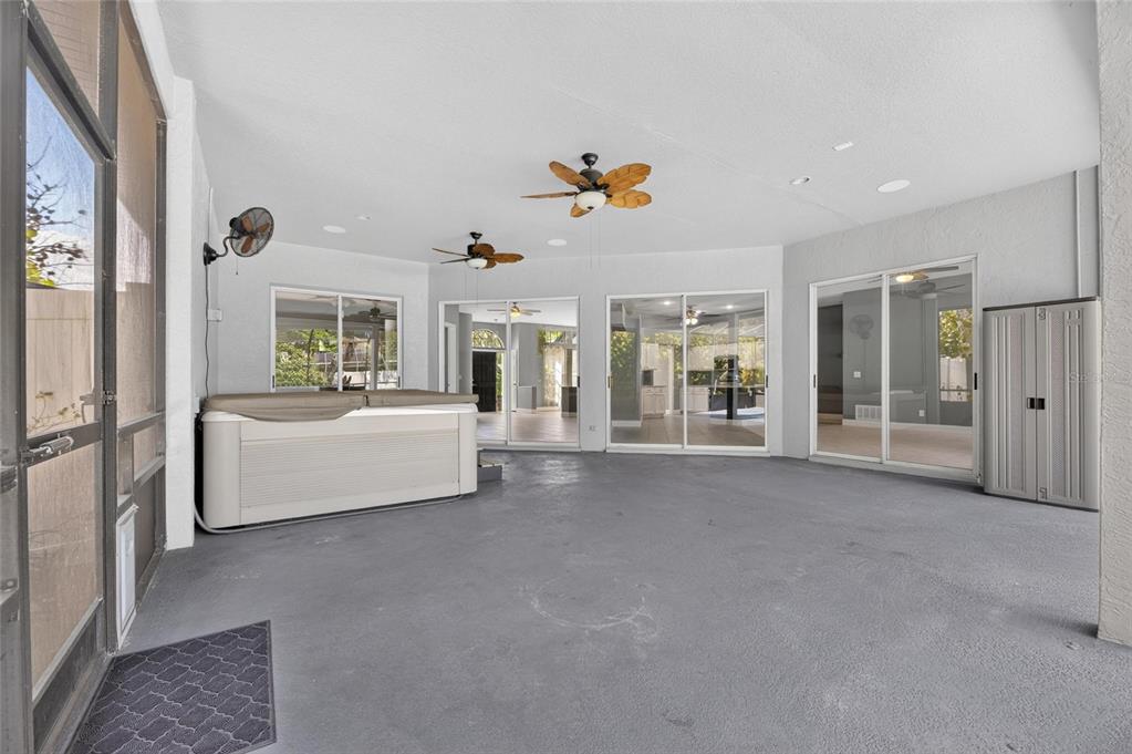 A covered patio features a hot tub, gray flooring, ceiling fans, and multiple sliding glass doors — 10409 HARVESTIME PLACE, RIVERVIEW, FL