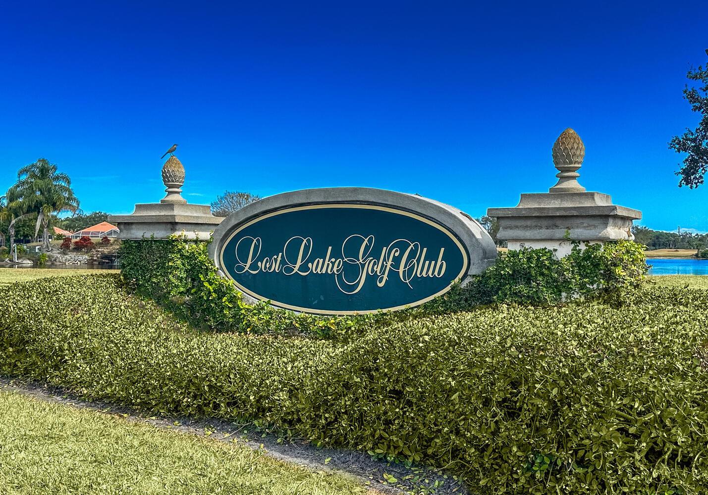 A stone sign for Lost Lake Golf Club sits behind a hedge under a blue sky — 8285 SE Double Tree Drive, Hobe Sound FL 33455, HOBE SOUND, FL