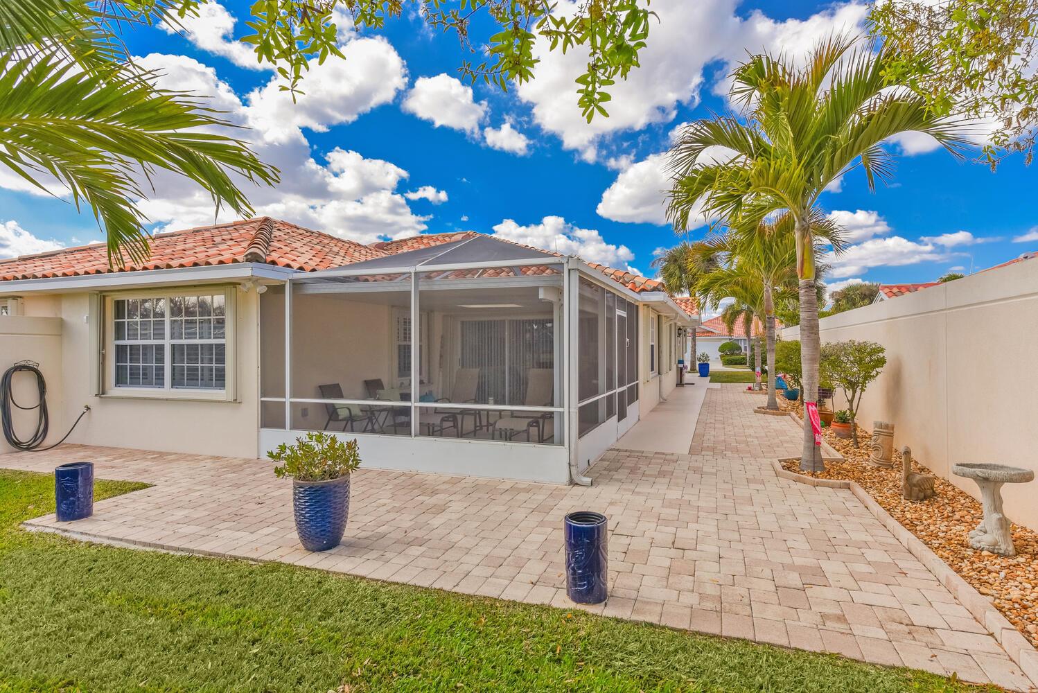 A patio with pavers and a screened-in porch sits beside a house with palm trees — 8285 SE Double Tree Drive, Hobe Sound FL 33455, HOBE SOUND, FL
