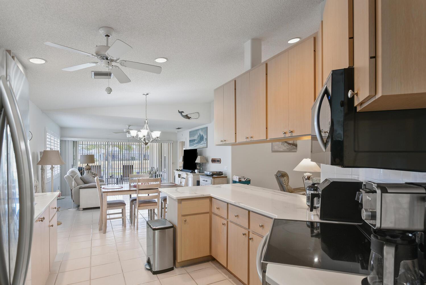 A kitchen with light wood cabinets and white countertops overlooks a dining and living area — 8285 SE Double Tree Drive, Hobe Sound FL 33455, HOBE SOUND, FL