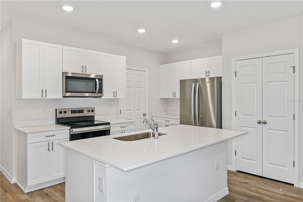 A kitchen features white cabinets, stainless steel appliances, a center island, and wood-look flooring — 9868 PELICAN COAST DRIVE, DADE CITY, FL