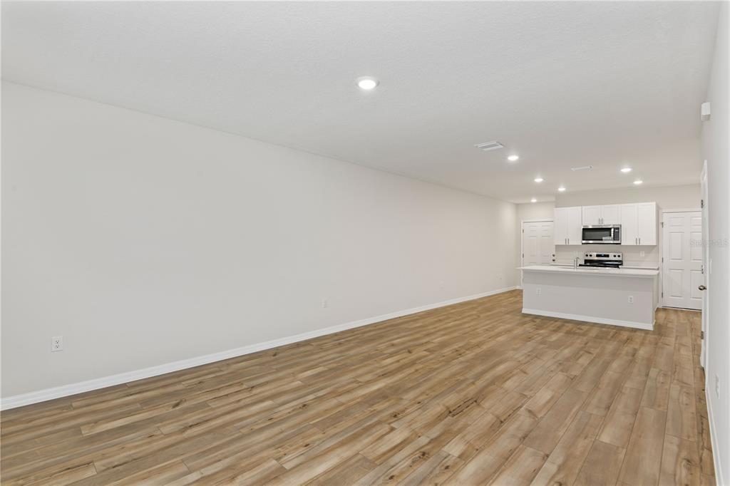 An open-concept living area features light-colored walls, wood-look flooring, and a kitchen with white cabinets — 9868 PELICAN COAST DRIVE, DADE CITY, FL