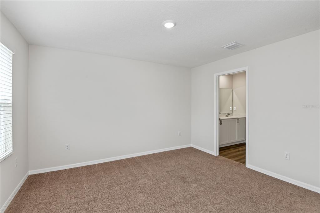 An empty bedroom features beige carpet, light-colored walls, a window, and an attached bathroom — 9868 PELICAN COAST DRIVE, DADE CITY, FL