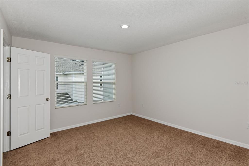 An empty bedroom features beige walls, brown carpeting, two windows with blinds, and a door — 9868 PELICAN COAST DRIVE, DADE CITY, FL