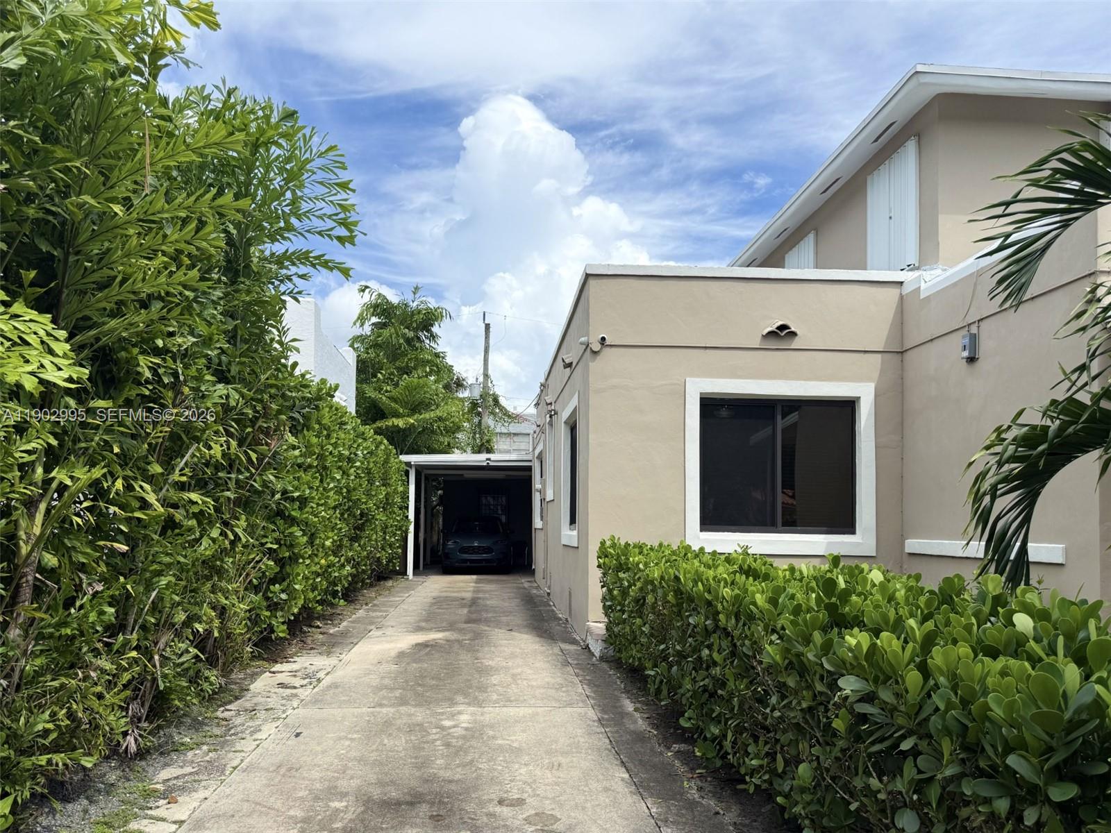 A concrete driveway leads to a covered carport beside a tan house with green hedges — 1835 SW 10th St, Miami FL 33135, MIAMI, FL
