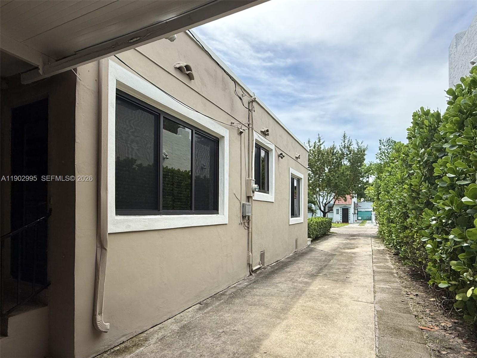 A beige exterior wall with windows and a downspout runs alongside a concrete driveway — 1835 SW 10th St, Miami FL 33135, MIAMI, FL